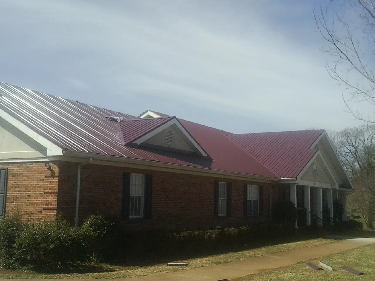 Red metal roof with gabled entries on a long brick building, from a Hail Damage Roof Repair job in Bridgewater