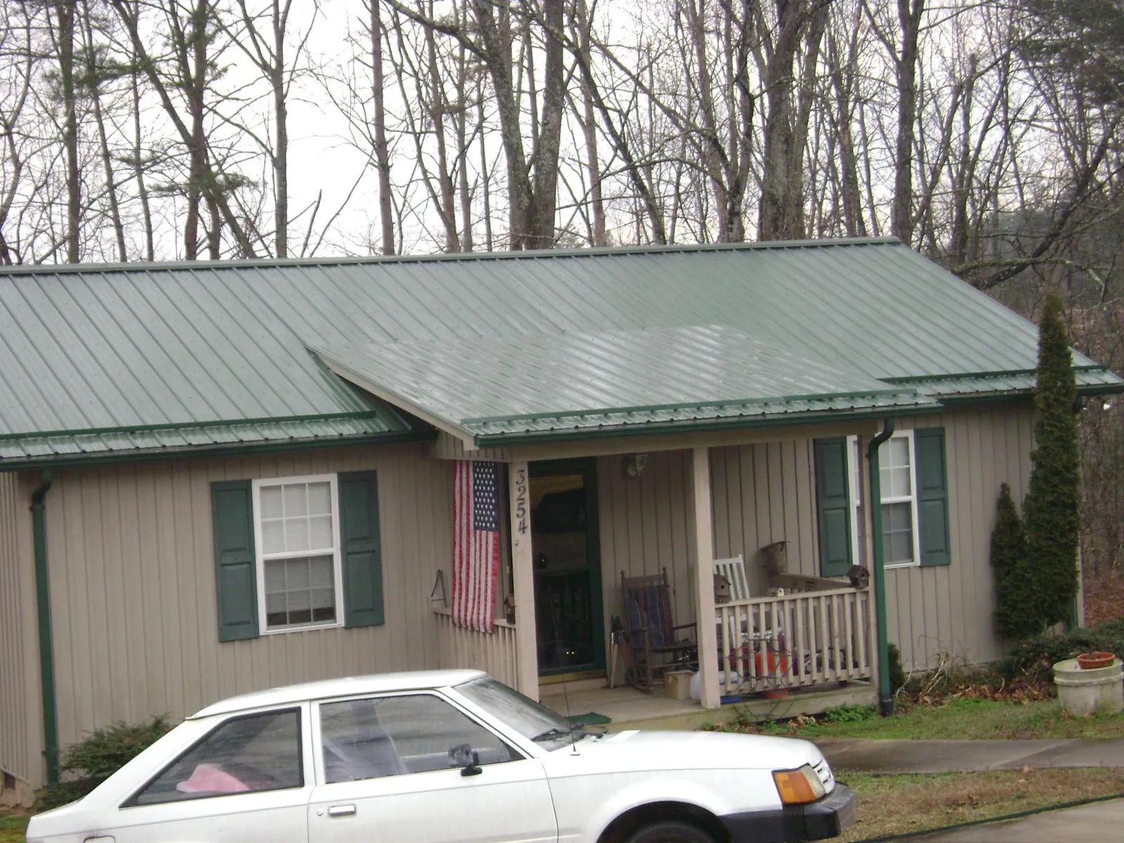 Green metal roof and front porch on a tan sided cottage in Bridgewater